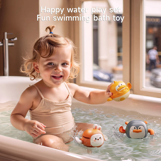 A smiling toddler in a beige swimsuit plays in a bathtub with three colorful wind-up swimming bath toys shaped like a duck, bunny, and penguin. The child is holding the yellow duck toy and splashing happily.