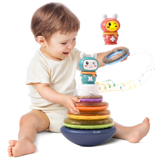 Colorful baby stacking rings toy with a musical feature. The toy includes a wobbling base, five translucent rainbow rings, and a cute bunny topper that can play music. One ring is shown separately with beads inside for sensory play.