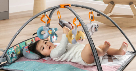 A baby lying on a colorful play mat, reaching for soft hanging toys attached to an arched activity gym.