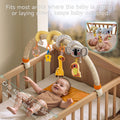 Baby lying in a crib smiling and reaching for a plush spiral arch toy featuring a koala head, giraffe, parrot, and rattles. Caption reads “Fits most areas where the baby is sitting or laying down, keeps baby occupied.” Crib size ≤80cm / 31.5 inch, with min clip ≈0.4 inch (1cm) and max stretch ≈2 inch (5cm) indicated.