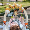 Baby lying in stroller looking up at giraffe-themed arch toy with plush hanging elephant teether, smiling monkey, green tree rattle, and bead ring. Image shows toy design from baby’s perspective for visual engagement and sensory play.