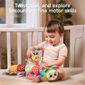 Toddler seated in crib twisting and pulling a small bee plush attached to a long multicolored caterpillar toy, demonstrating fine motor skill exploration