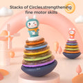 Two colorful stacking rings toys with wobbling bases, each topped with a bunny character. The toys feature translucent rainbow-colored rings stacked in order, designed to strengthen babies’ fine motor skills. The background includes soft pastel elements such as arches, clouds, and a windmill for a playful, child-friendly atmosphere. Text on the image reads: “Stacks of Circles, strengthening fine motor skills.”