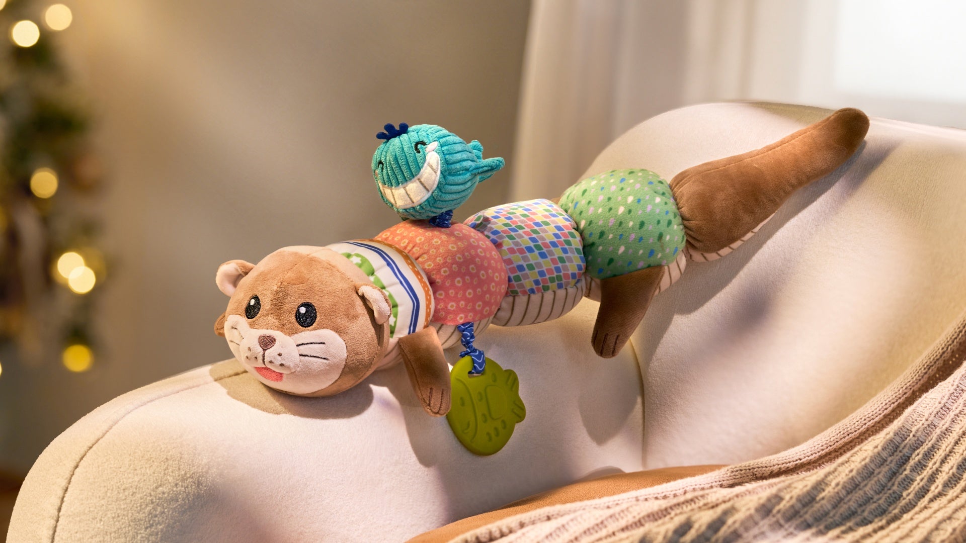 Video shows baby playing with multi-functional otter-shaped sensory toy, featuring a cute blue whale teether and green leaf-shaped teether attachment. Toy is made of colorful fabric segments and includes a brown plush head, multi-color patterned body and tail.