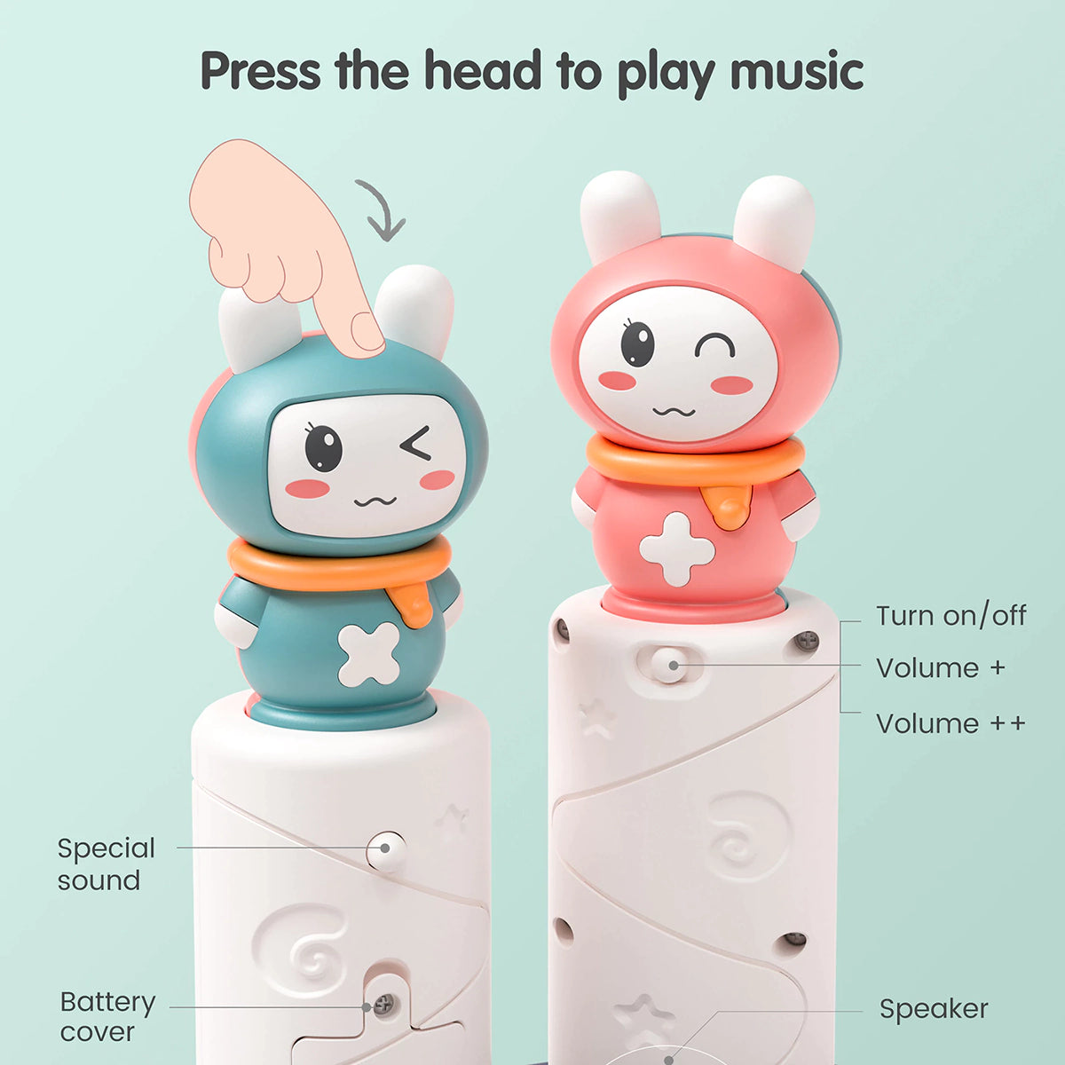 Close-up of two bunny toppers from the baby musical stacking rings toy, one in teal and one in pink. The bases show labeled features including power button, volume controls, speaker, special sound button, and battery cover.
